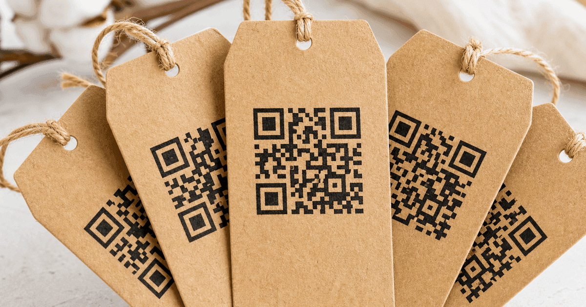 Cinq produits différents alignés sur un établi, chacun portant son étiquette volante à QR code sous une lampe de bureau à lumière chaude